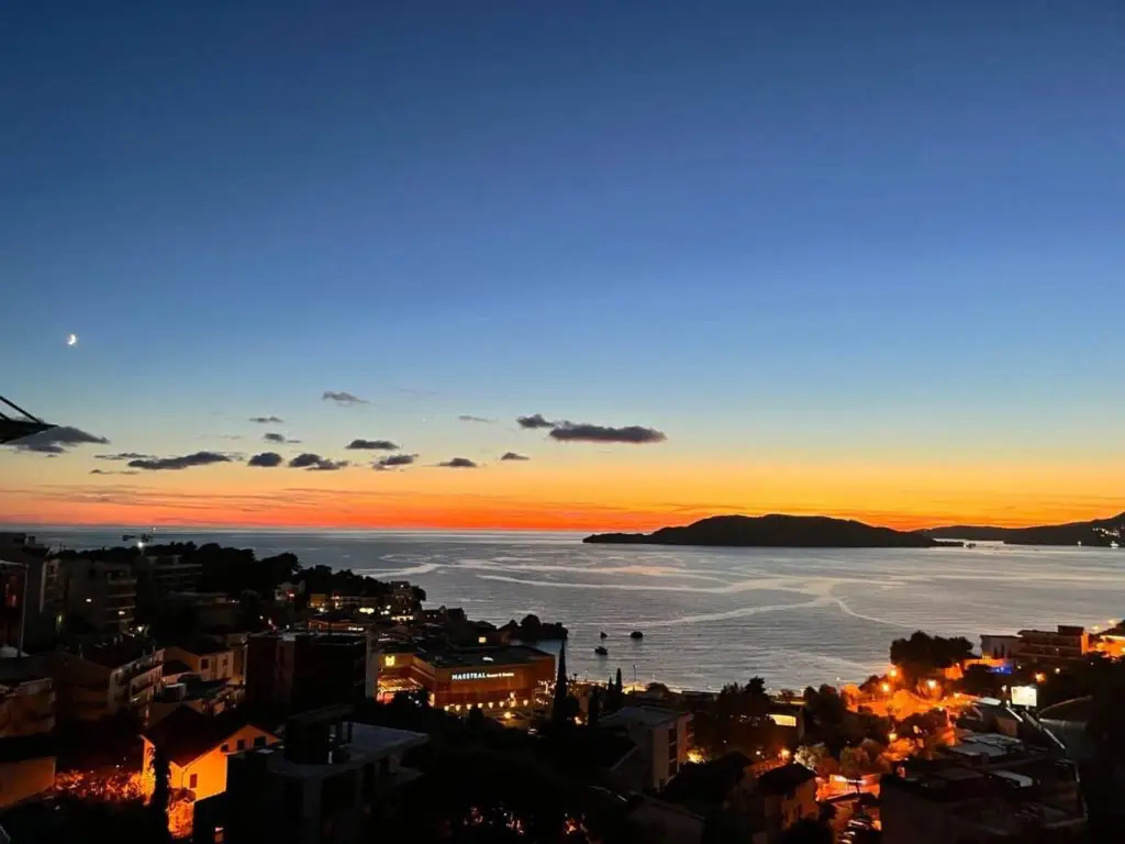Sunset over sea with island silhouette and town lights