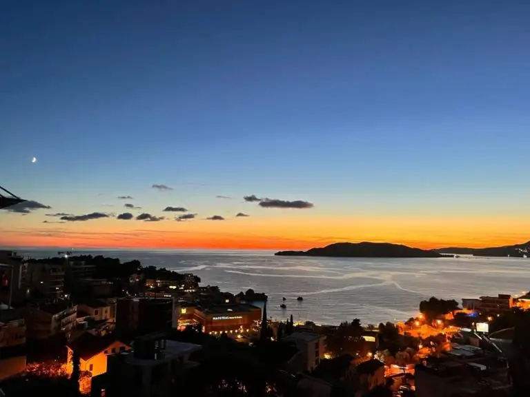 Sunset over sea with island silhouette and town lights