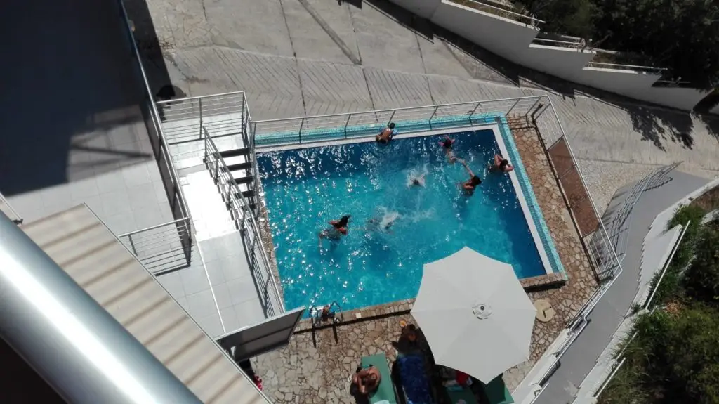 Overhead view of outdoor pool with several swimmers and white umbrella
