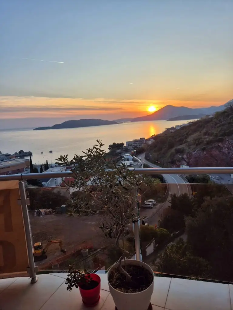 Balcony view of sea sunset, mountains, road, and potted plants