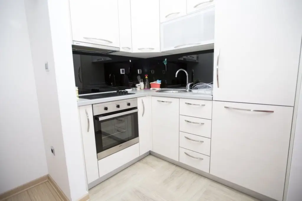White corner kitchen with black backsplash and built-in oven