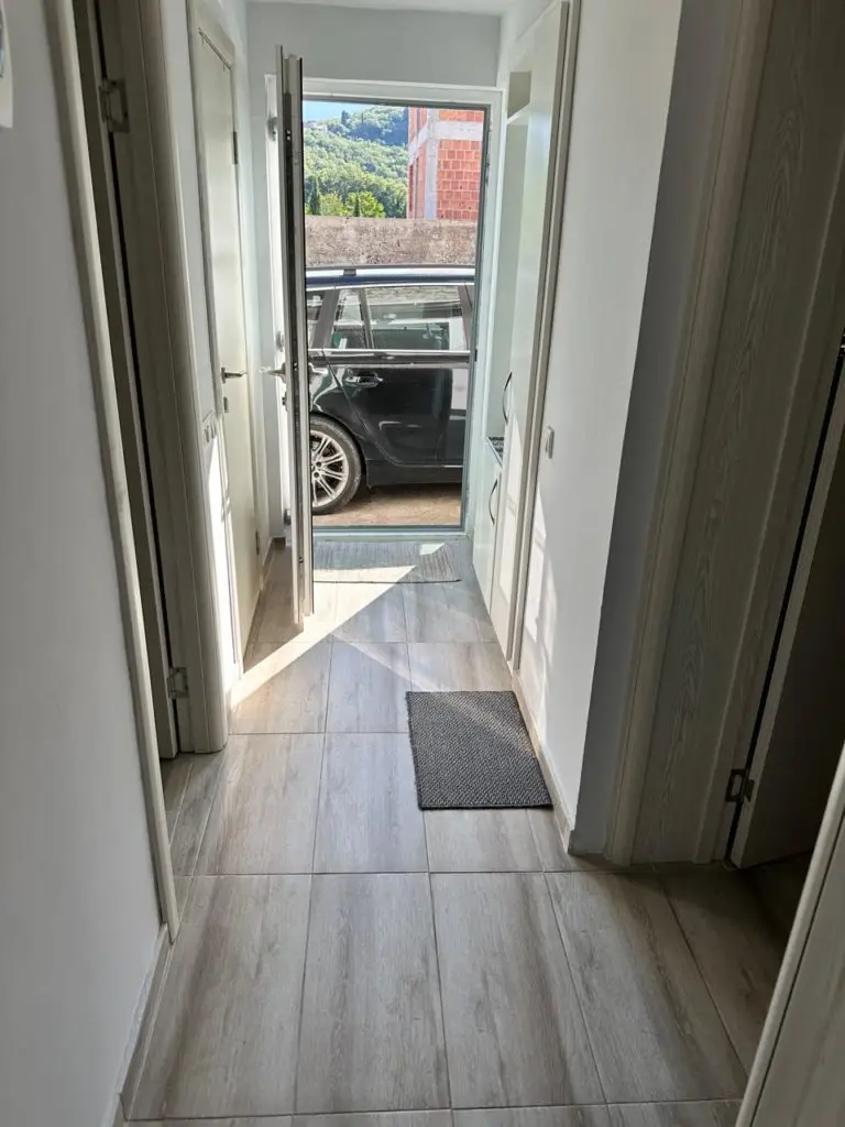 Narrow hallway with tiled floor, open door, and parked black car outside