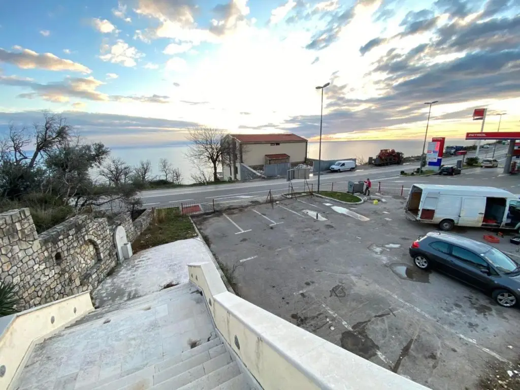 Coastal parking lot beside road, gas station, and sea at sunset