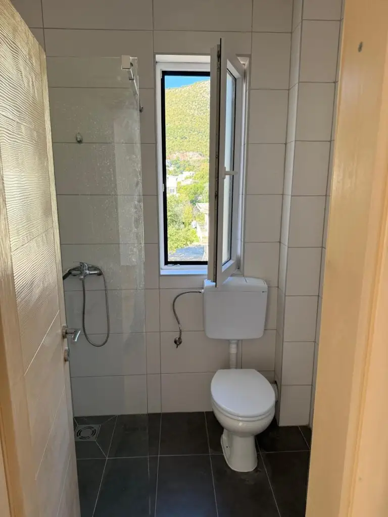 Small tiled bathroom with toilet, shower, and open window