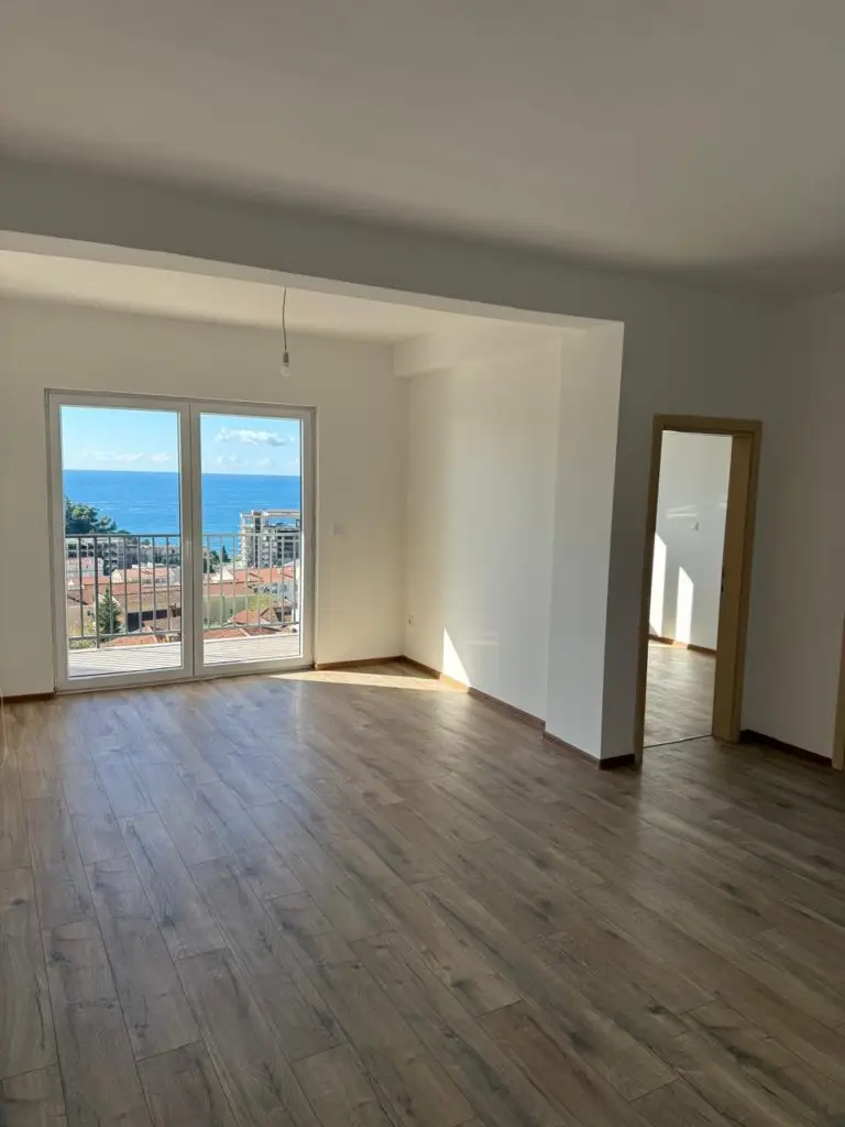 Empty apartment room with wood floor and sea view through balcony doors