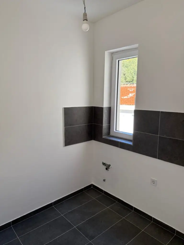 Unfinished kitchen corner with black tile floor and wall tiles, window, and hanging bulb