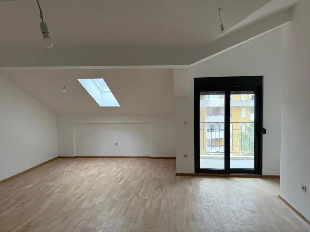 Empty attic room with skylight, wooden floor, and balcony door