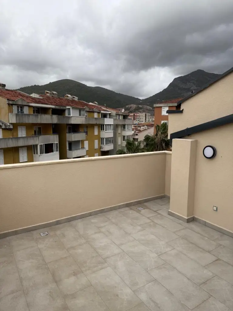 Tiled rooftop terrace with beige walls, buildings, and mountains beyond