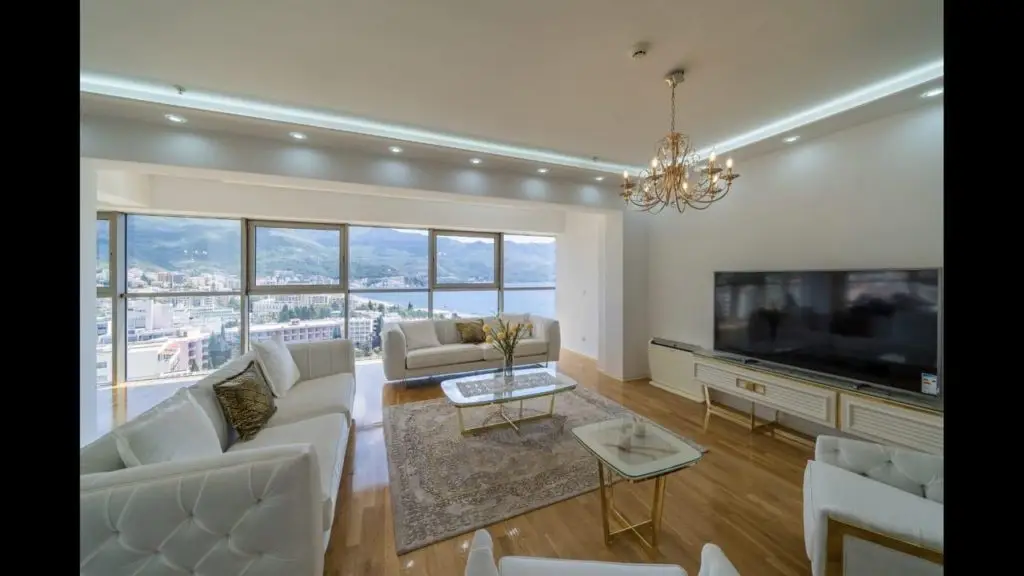 Bright living room with white sofas, TV, and bay view