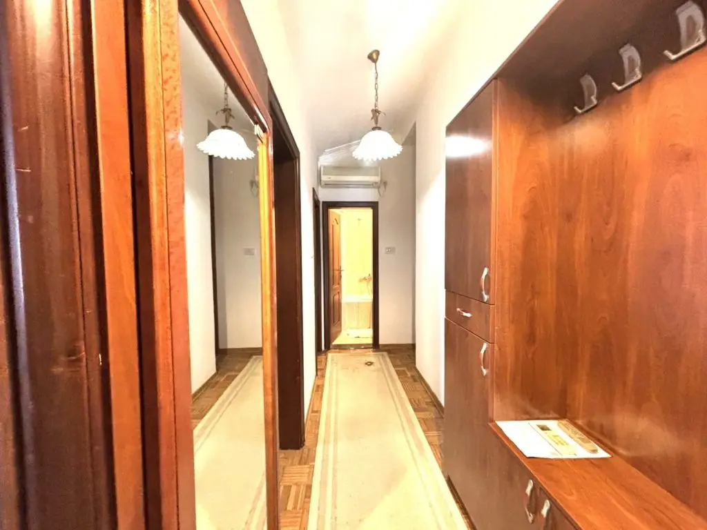 Narrow hallway with wooden cabinets, mirror, and hanging lights