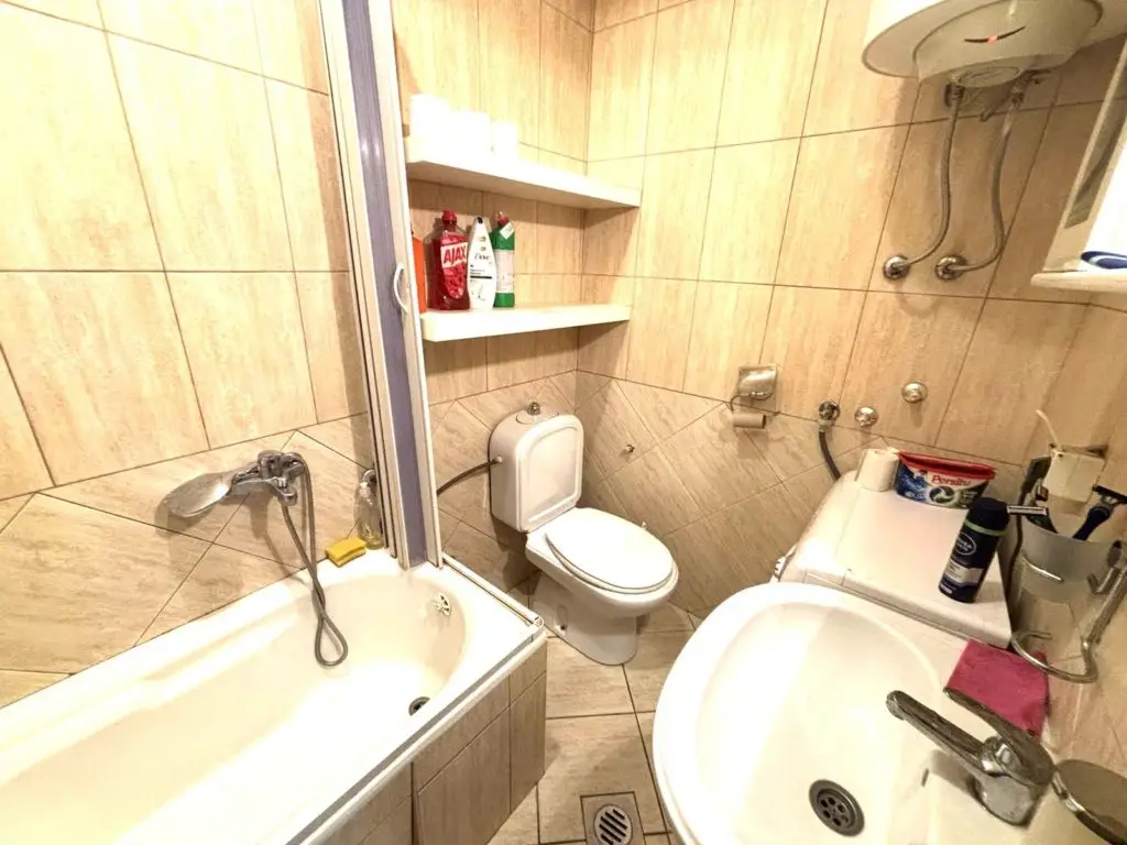 Small beige-tiled bathroom with bathtub, toilet, and sink
