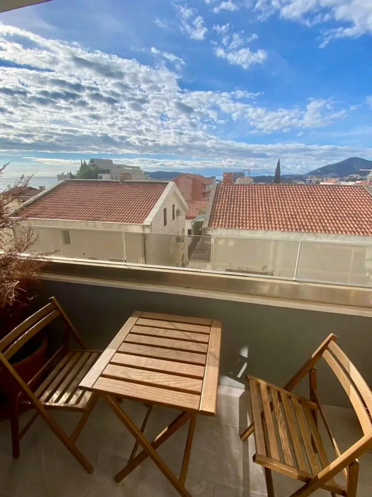 Balcony with wooden table and chairs overlooking rooftops and sea