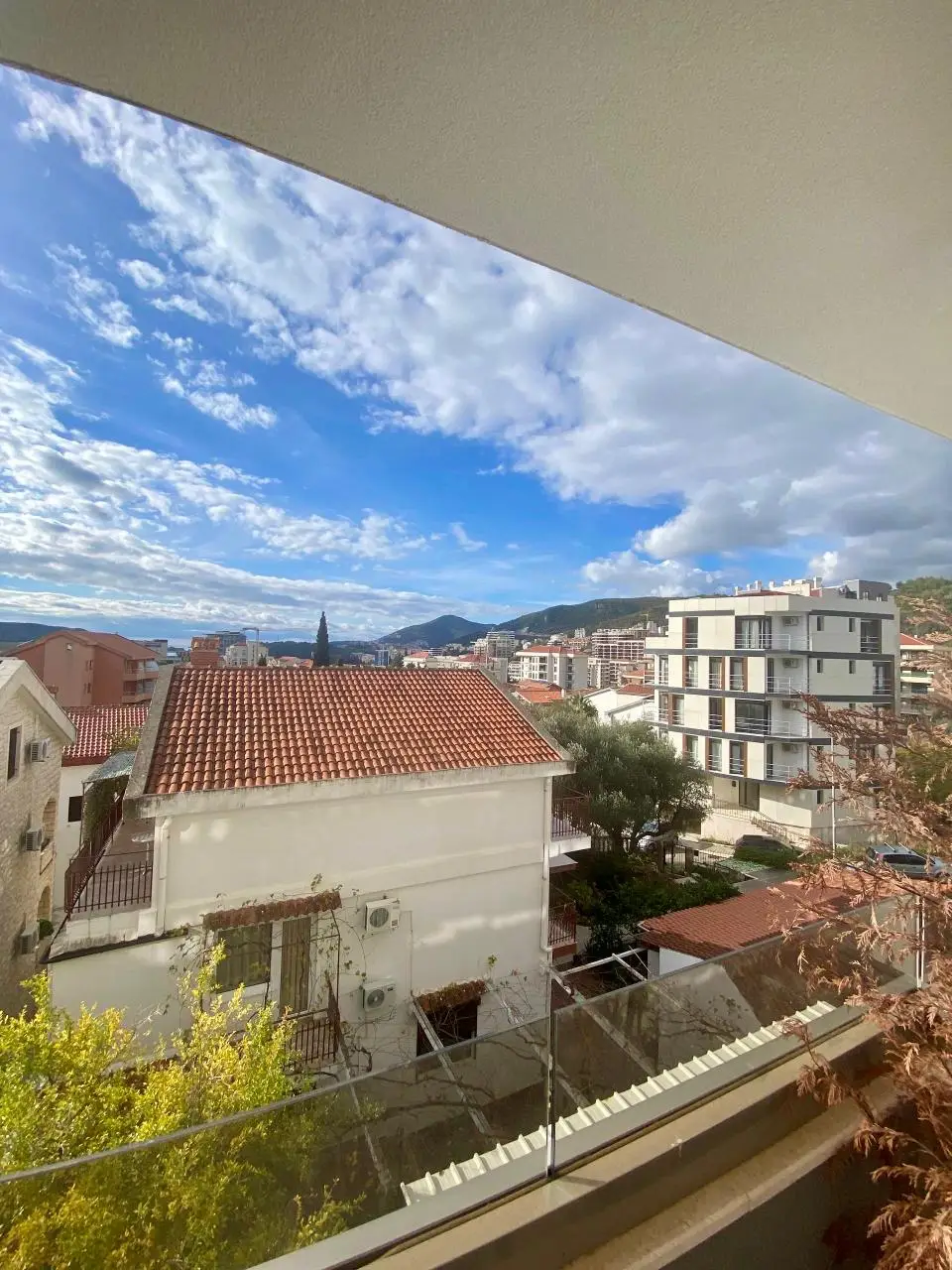 Balcony view over rooftops, buildings, mountains, and cloudy sky