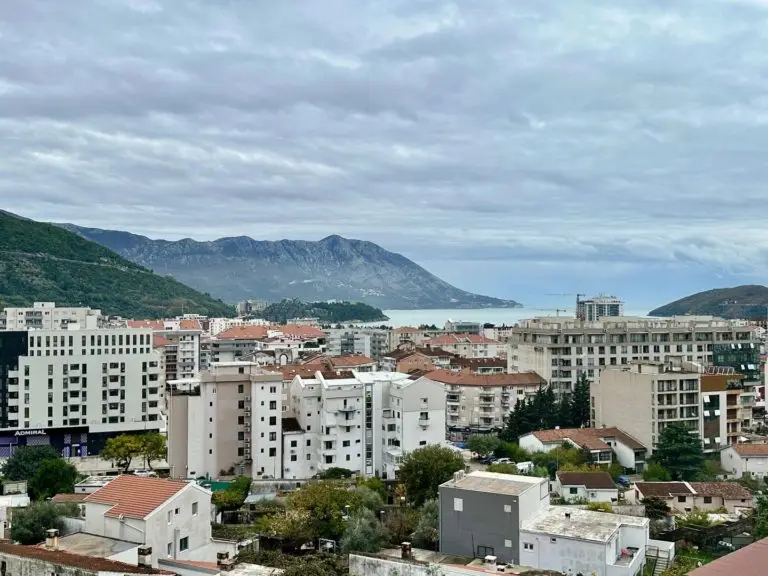Cityscape with apartment buildings, bay, and mountains under cloudy sky