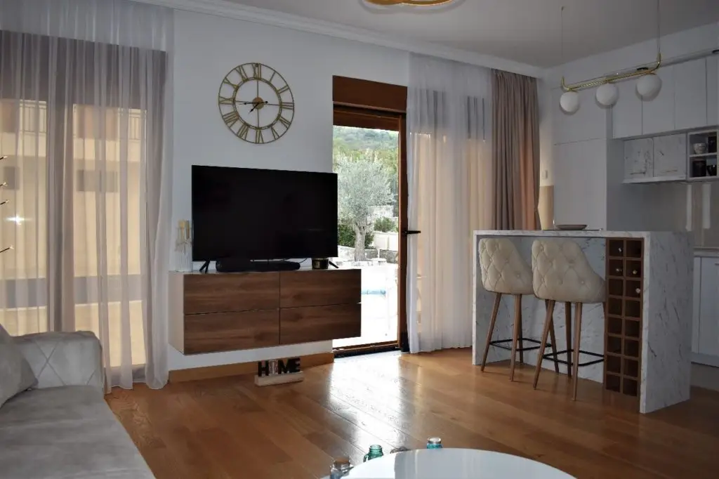 Modern living room with TV, clock, bar stools, and kitchen