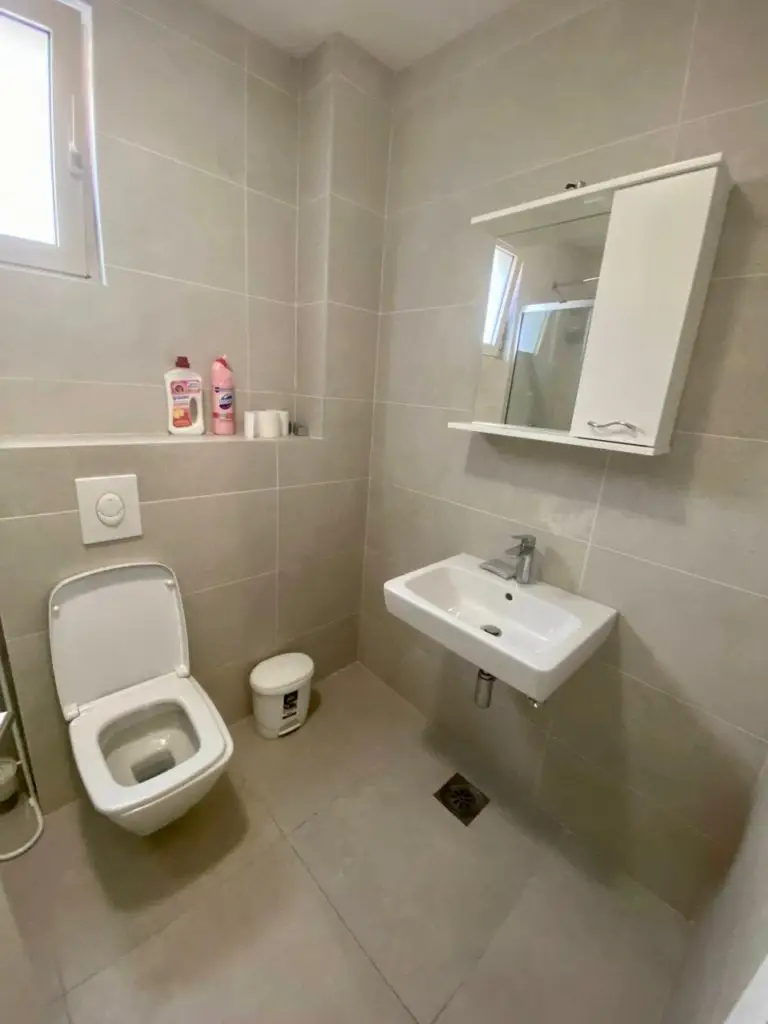 Small beige tiled bathroom with toilet, sink, and mirror cabinet