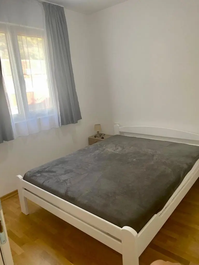Bedroom with white bed, gray blanket, and window curtains