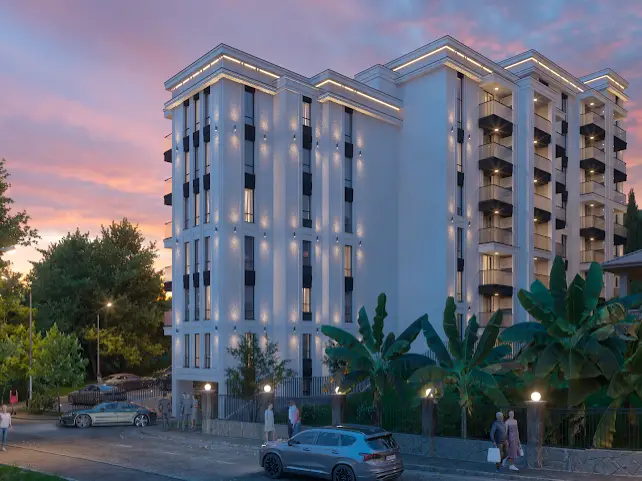 White apartment building with balconies at dusk, surrounded by trees