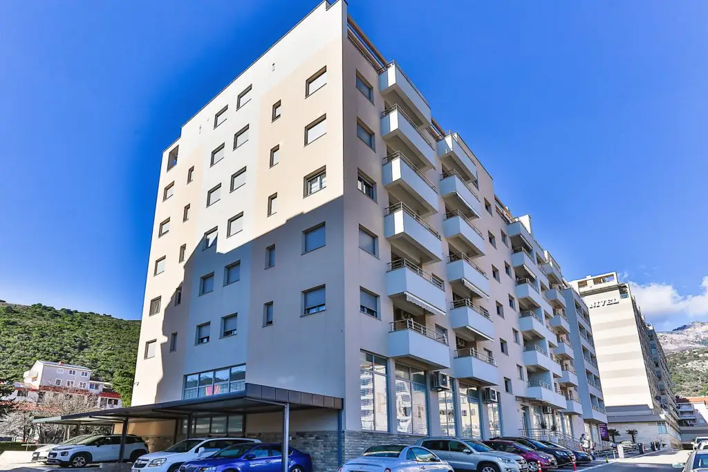 Large beige apartment building with balconies and parked cars