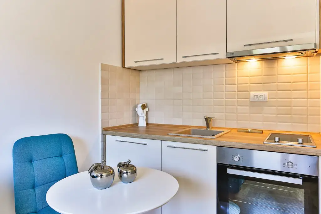 Compact kitchen with blue chair, round white table, and built-in oven