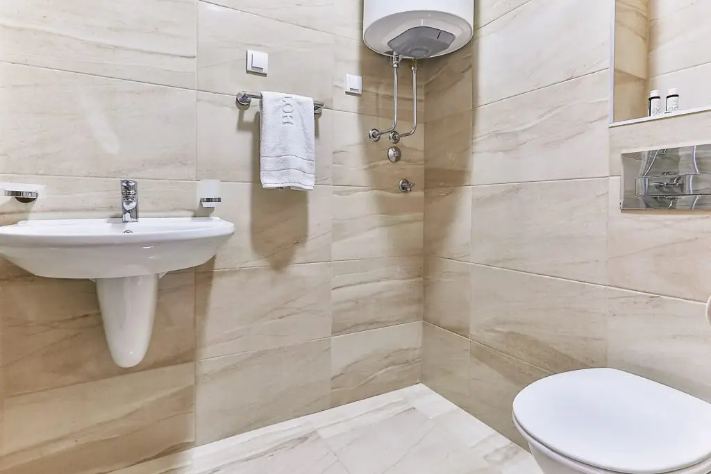 Compact beige-tiled bathroom with sink, shower, and toilet