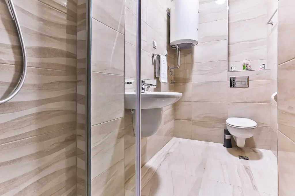 Modern beige bathroom with shower, sink, toilet, and water heater