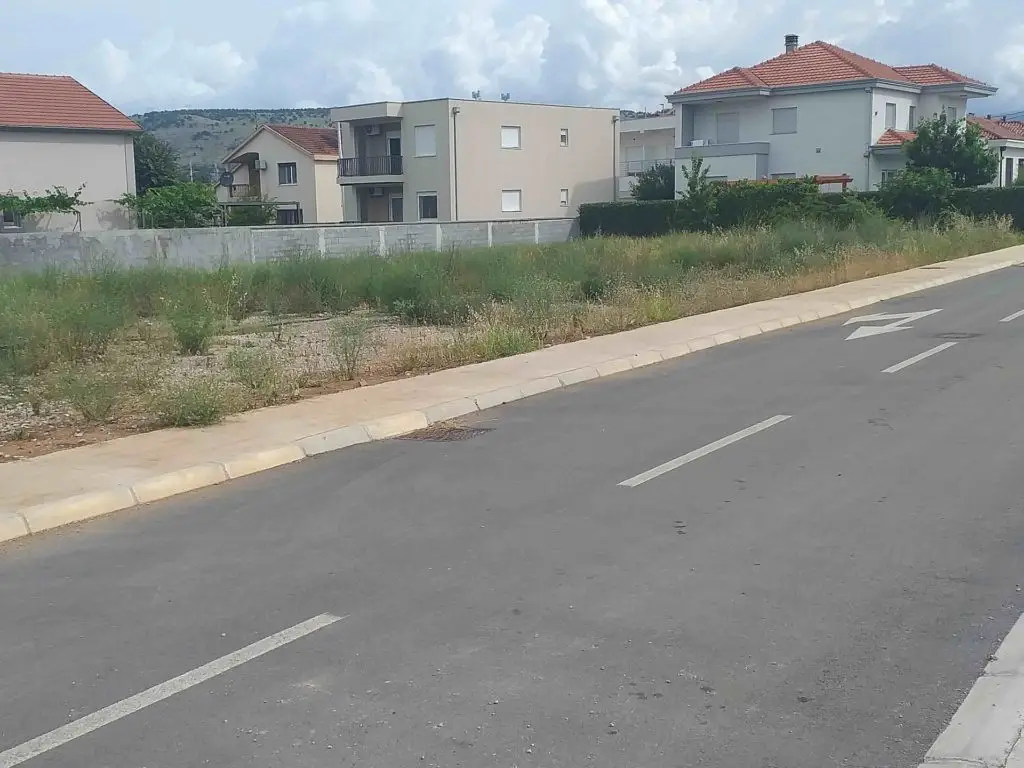 Paved road beside grassy vacant lot and houses