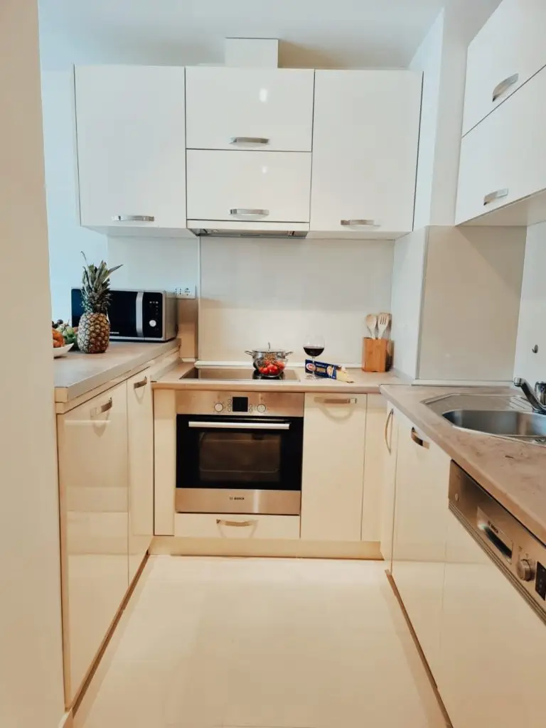 Compact white kitchen with oven, sink, microwave, and pineapple