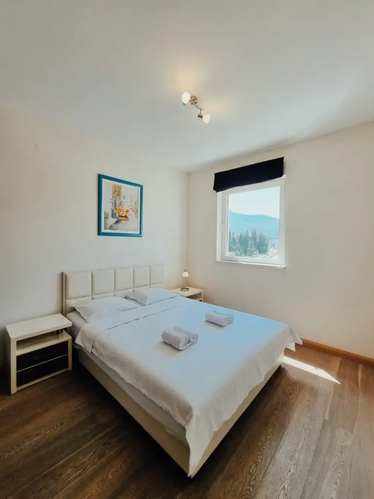 Bright bedroom with white bed, bedside tables, and window view