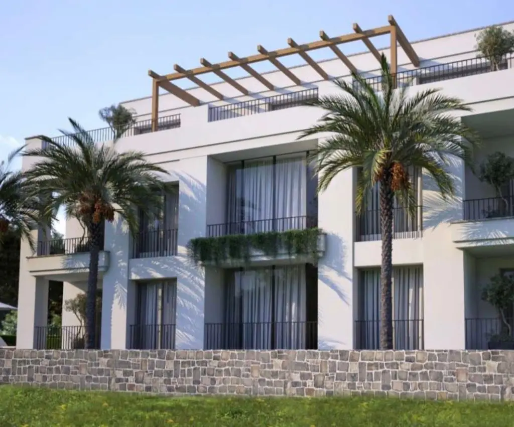 Modern white apartment building with palm trees and stone wall
