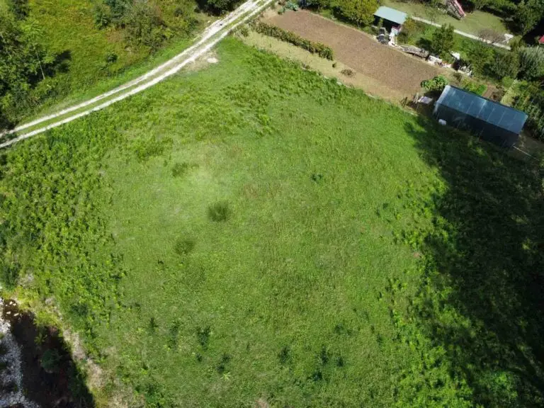 Aerial view of a grassy vacant lot with dirt path and shed