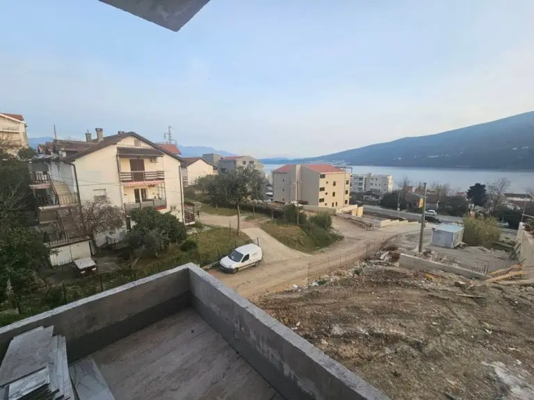 Balcony view over houses, road, and sea with hills