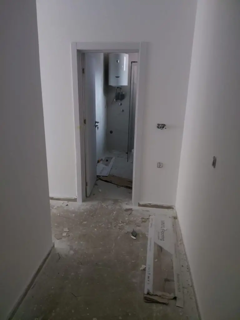 Unfinished hallway with open door to small bathroom and boiler