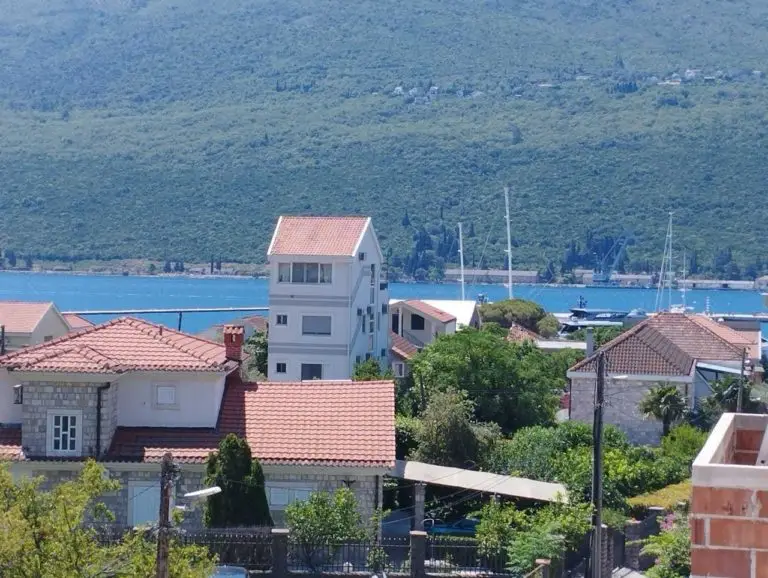 Houses with red roofs overlooking a blue bay and green hillside