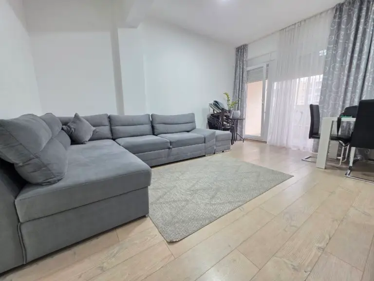 Gray sectional sofa in a bright living room with dining table, rug, and balcony doors